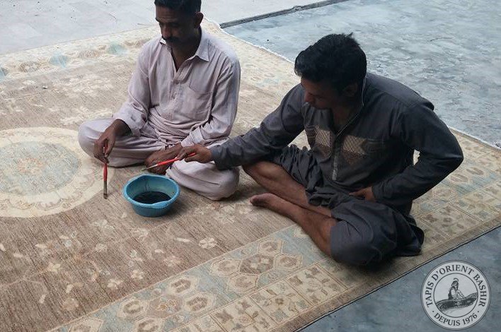 Des artisans pakistanais retouchent un tapis avec des colorants naturels.